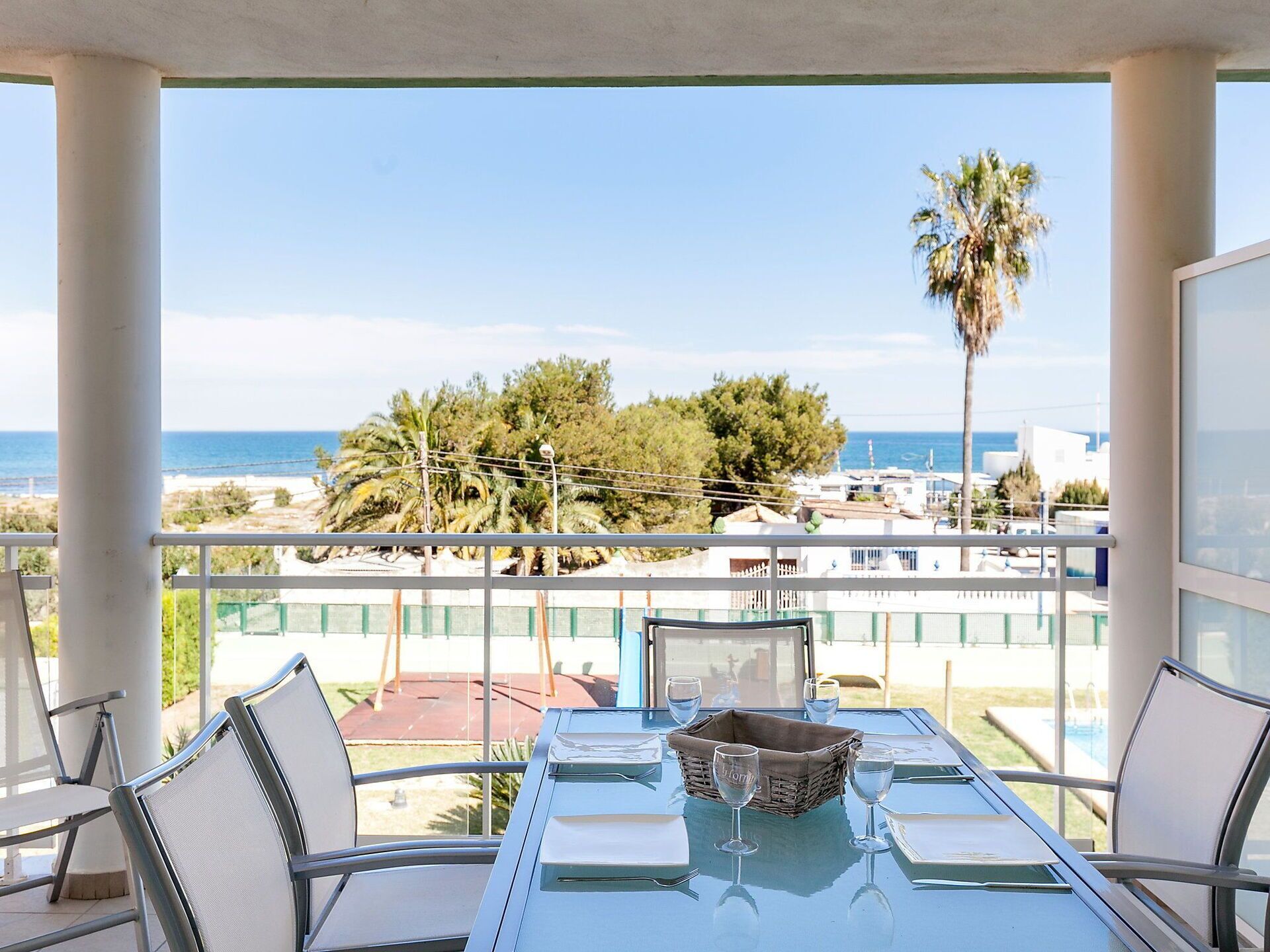 Uma varanda com uma mesa posta para dois, com vista para a praia e palmeiras.