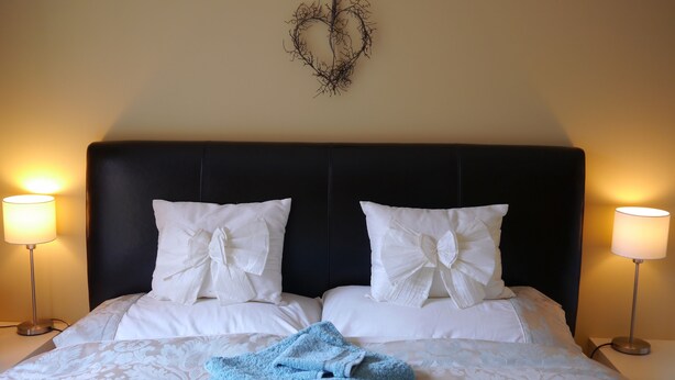 A neatly made bed with white linens and two pillows, a blue towel, and a wall-mounted decorative piece above. - York city centre apartment, North Yorkshire, England (York)