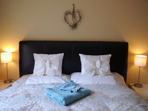 A neatly made bed with white linens and two pillows, a blue towel, and a wall-mounted decorative piece above.