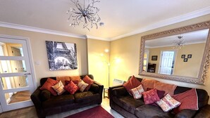 A living room with two dark brown sofas, a red carpet, a chandelier, a large mirror, and a painting of a bridge. - York city centre apartment, North Yorkshire, England (York)