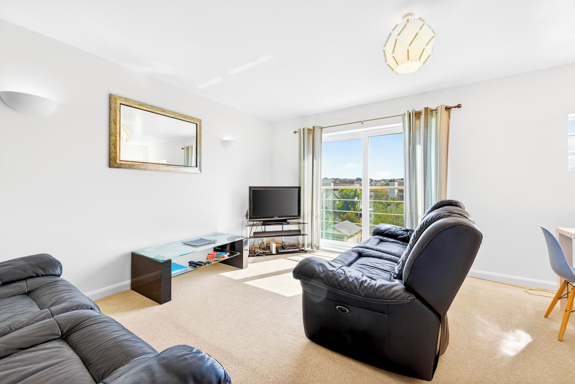 Ein modernes Wohnzimmer mit einer Couch, einem Fernseher, einem Glastisch und Blick ins Freie.