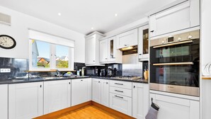 A modern kitchen with white cabinets, a Bosch oven, and a window with a view of houses. - Modern well equipped townhouse, 3 min walk from Crooklets Beach, Bude (Bude)