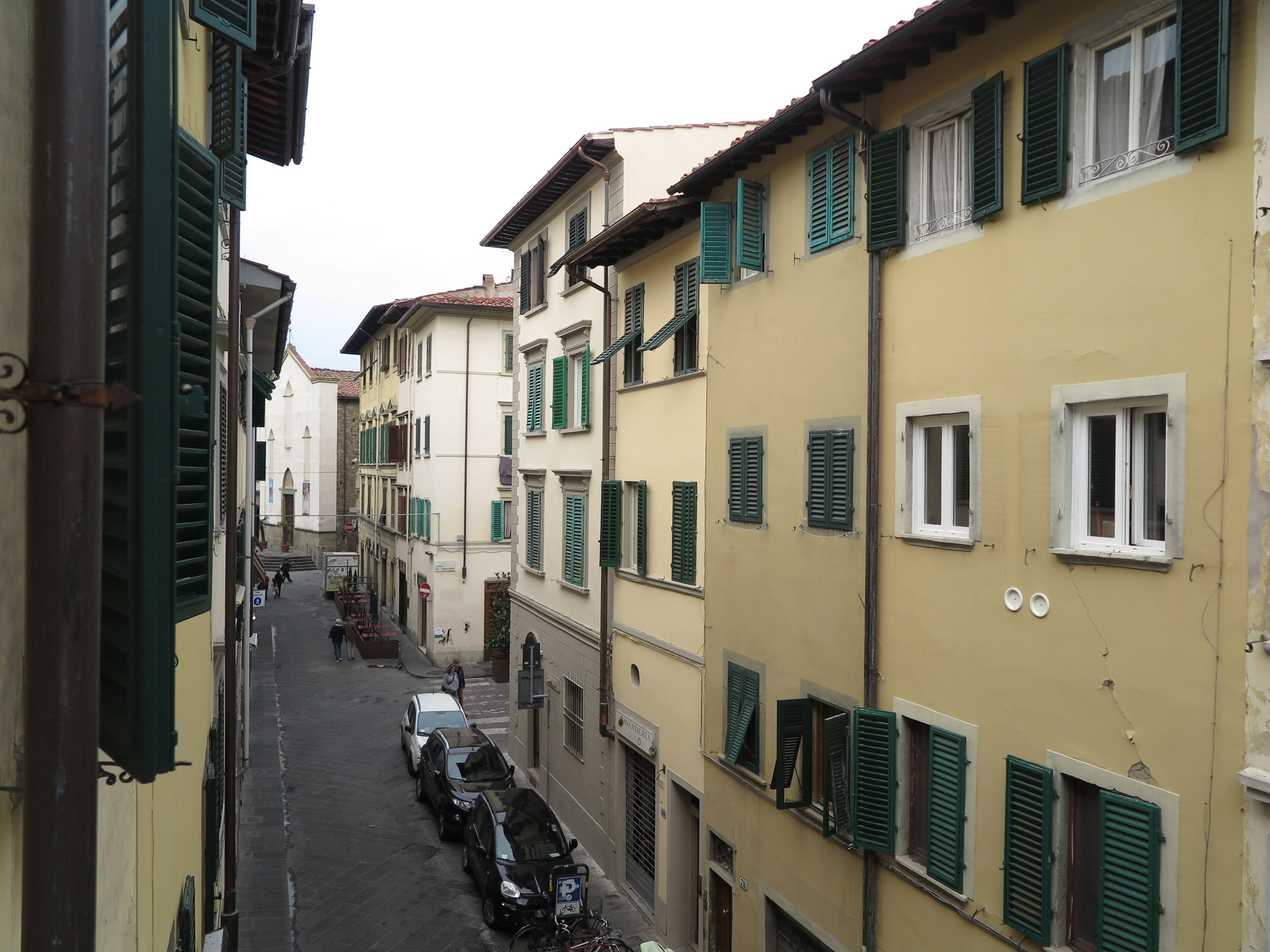 A narrow street lined with multi-story buildings, each with green shutters and a mix of architectural styles.