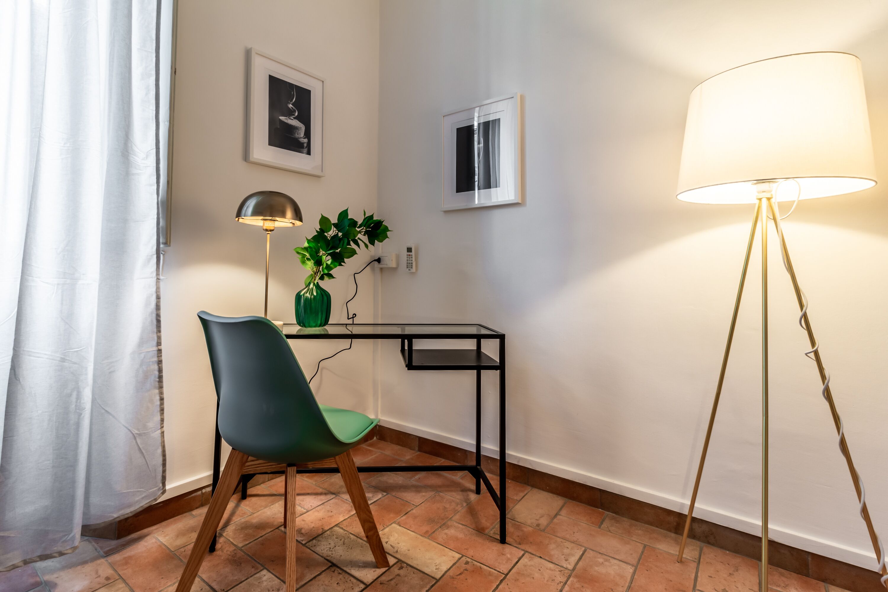 A room with a desk, chair, lamp, and potted plant.