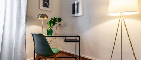 A room with a desk, chair, lamp, and potted plant.