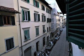 A narrow street with parked cars and buildings with green shutters.