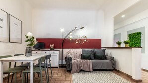 A compact living space with a dining area, a sofa, a decorative wall, and a small plant arrangement.