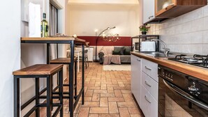 A compact kitchen with a wooden countertop, a built-in oven, and a sink. There is a dining area with a table and chairs, and a sofa in the background.