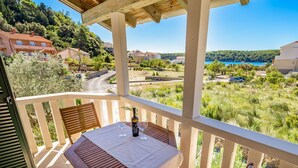 A balcony with a table and chairs, overlooking a coastal landscape with houses and a road.