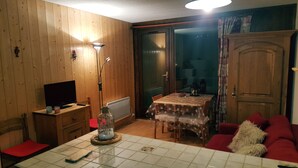A cozy living room with wooden walls, a dining table with a tablecloth, a red sofa, and a television on a wooden cabinet. - Magnificent view ! Vallouise, Parc des Ecrins, Puy st Vincent, Pelvoux Hautes Alpes (Vallouise)