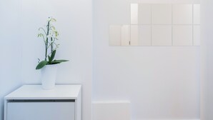 Una stanza bianca con un'orchidea in vaso su un tavolo bianco e uno specchio a parete.