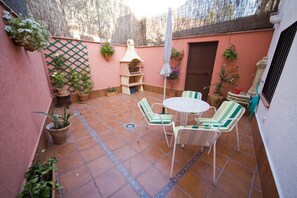 A patio with a round table and chairs, potted plants, and a grill.