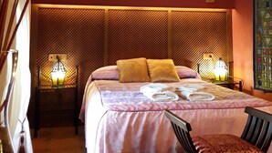 Un dormitorio con una cama, dos lámparas de noche, una silla y un adorno de pared.