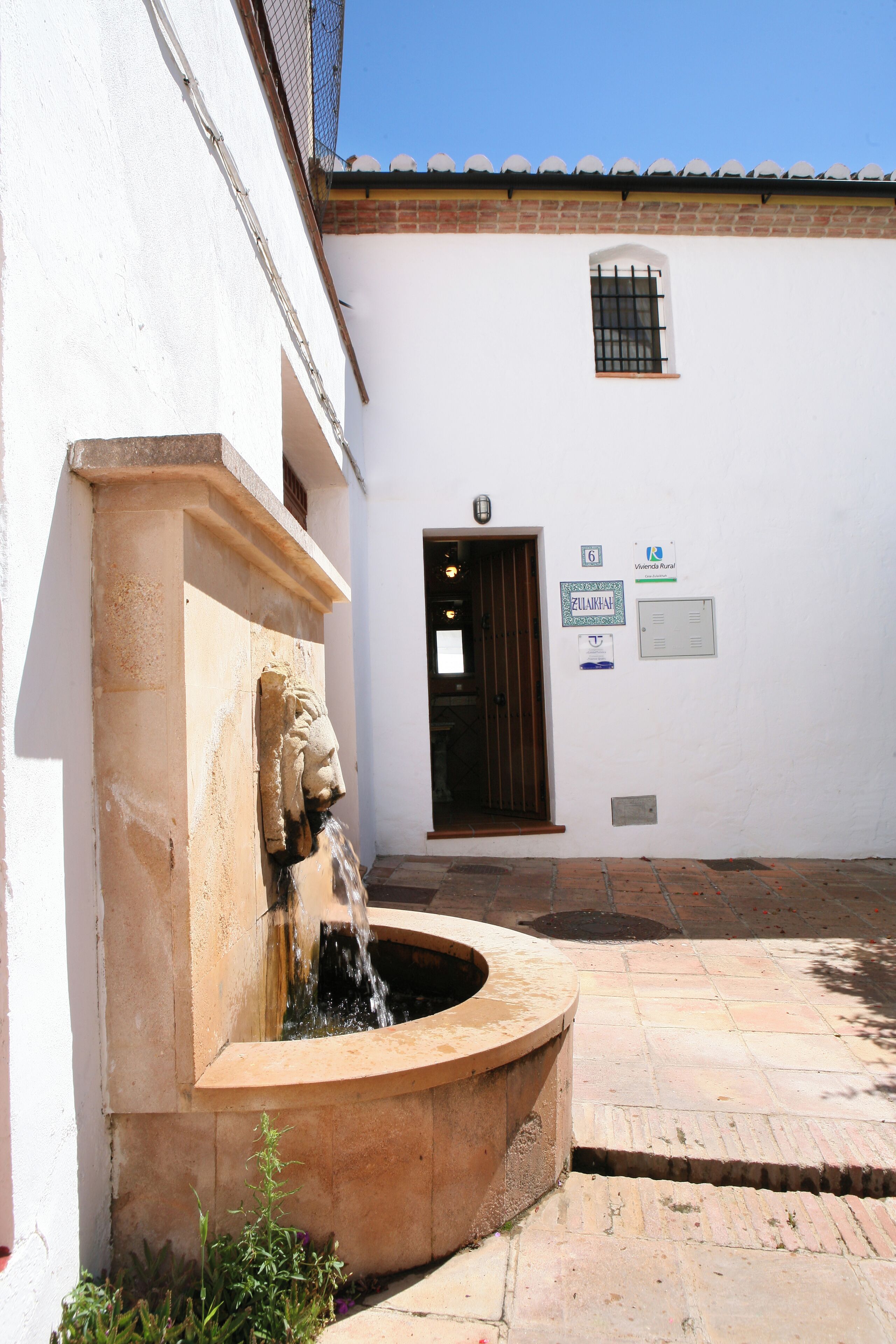 A courtyard with a fountain, a white building with a door, and a window.