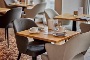 Un comedor de hotel con mesas preparadas para dos, sillas y un menú.