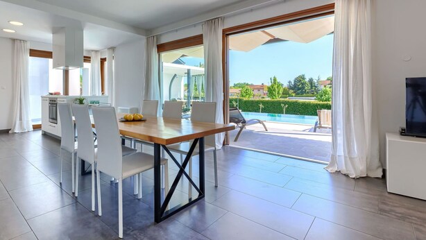 Uma sala de estar moderna com área de jantar, janelas amplas e vista para uma piscina.