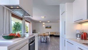 Uma cozinha moderna com armários brancos, forno embutido e um espaço de refeições com mesa e cadeiras.