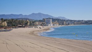 Ein weiter Sandstrand mit blauem Meer und Bergen im Hintergrund.