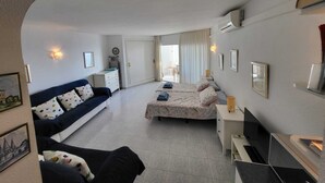 Ein kleines Hotelzimmer mit Bett, einer Couch, einem Schreibtisch und einer kompakten Küchenzeile.