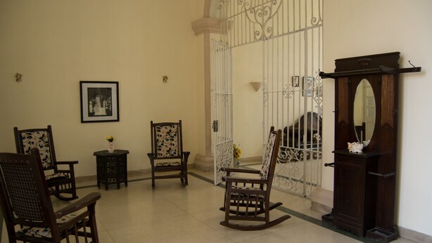 A room with a wooden rocking chair, a small table with a vase, and a mirror on a stand. - Hostal Sagrada Familia (Matanzas)