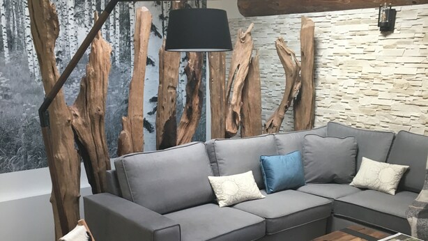 Uma sala de estar moderna com um sofá seccional cinza, uma mesa de centro de madeira e uma poltrona com encosto de couro.