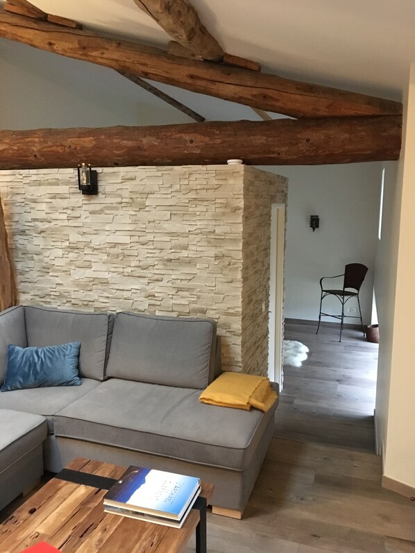 A cozy living room with a grey sectional sofa, a wooden coffee table, and a stone wall.