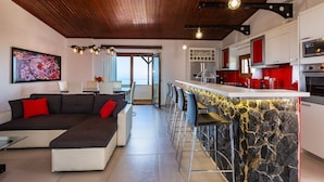 Una cocina moderna con una isla de piedra, detalles en rojo y un techo de madera.