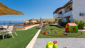 Zona de piscina con sillones reclinables, área de juegos para niños y vista al mar.