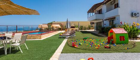 A pool area with lounge chairs, a children's play area, and a view of the sea.
