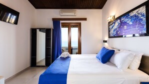 Habitación de hotel con cama, un cuadro en la pared, televisor y vista al mar a través de una puerta.