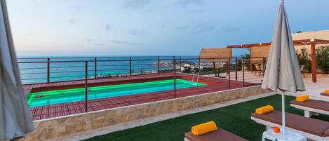 Une piscine sur le toit avec vue sur la mer, des chaises longues et une pergola.