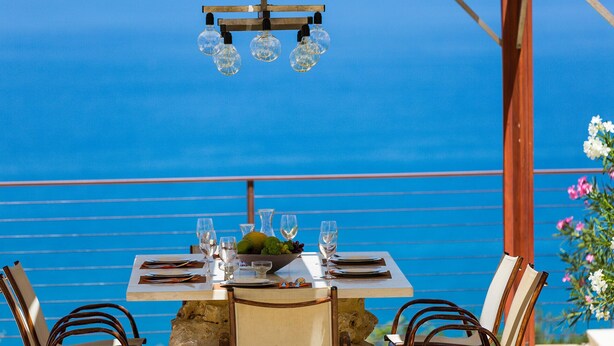 Mesa lista para comer con vista al mar, una lámpara de techo de madera y sillas con base de piedra.