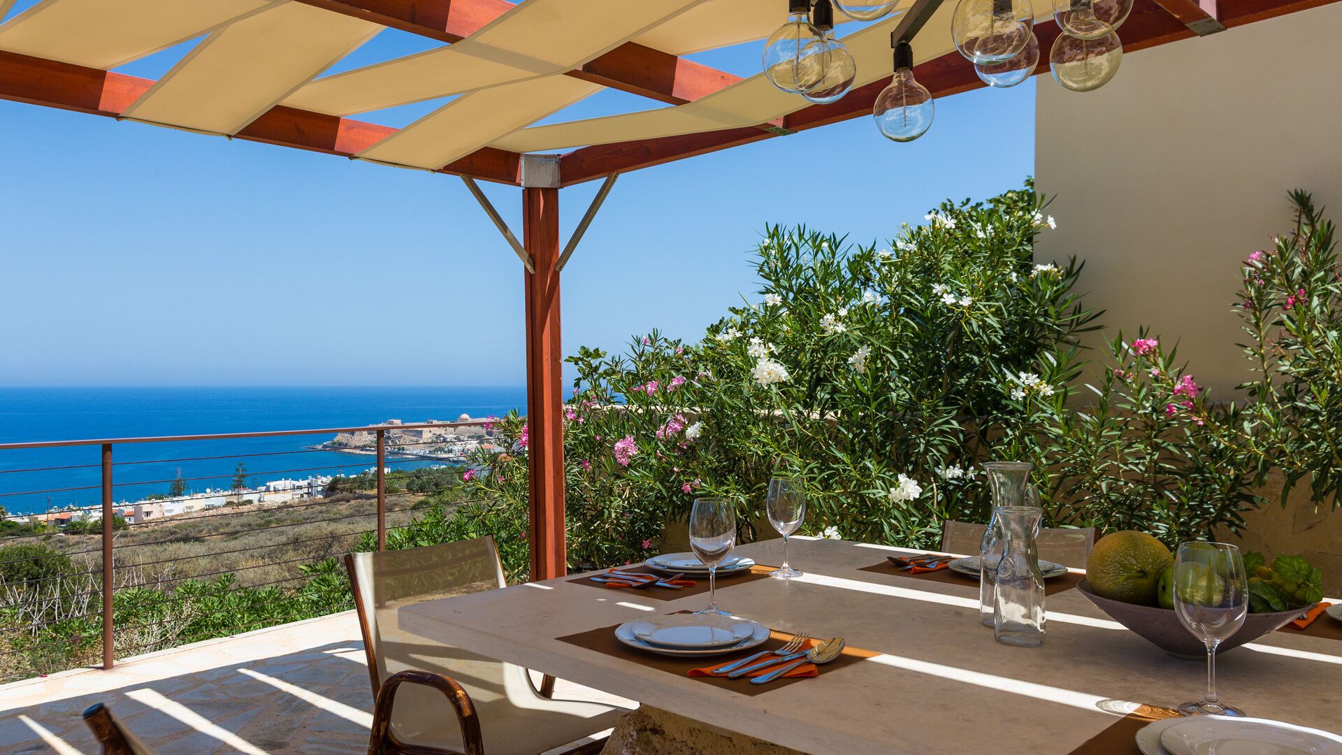 An outdoor dining area with a table set for two, overlooking a coastal view.