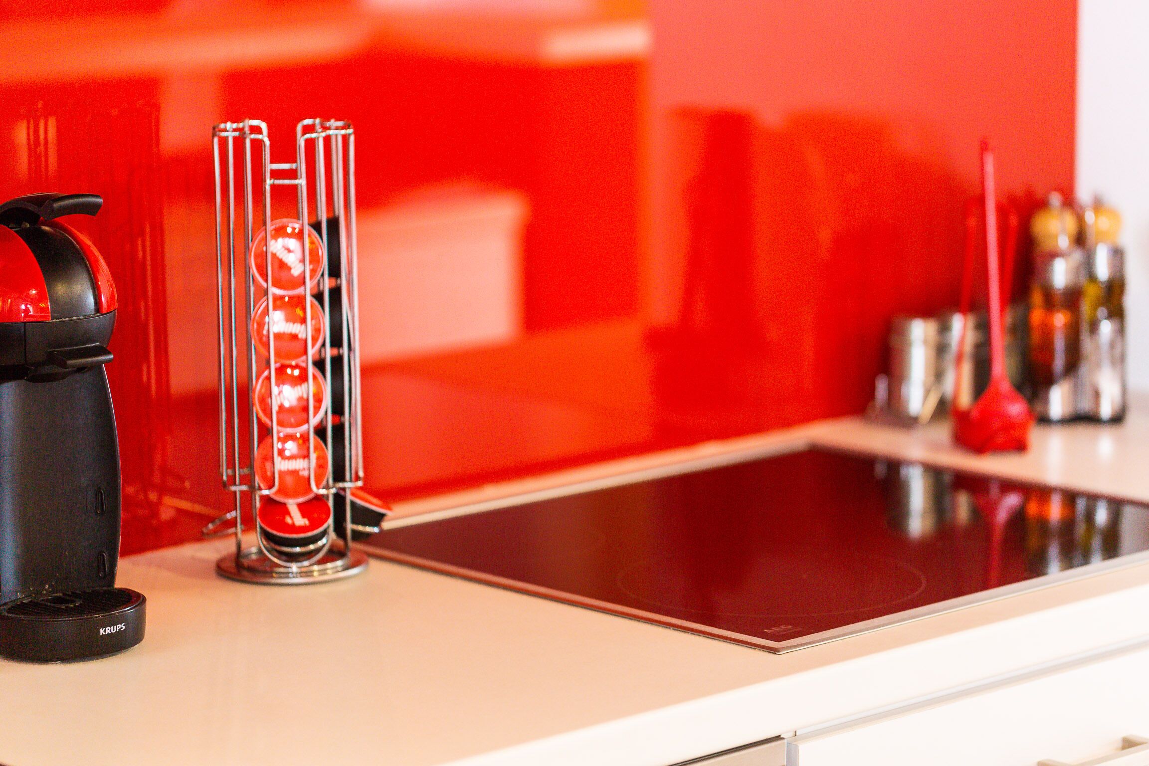 A kitchen with a red backsplash, a coffee maker, and a glass carafe with a red liquid.