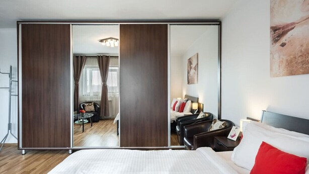Ein modernes Hotelzimmer mit einem großen Bett, einem Spiegel, einem Schreibtisch und einer Sitzecke mit Sessel und Tisch.