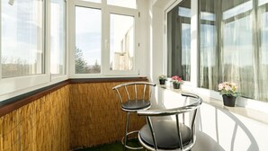 Ein Eckbalkon mit Tisch und zwei Stühlen, großen Fenstern und Topfpflanzen.