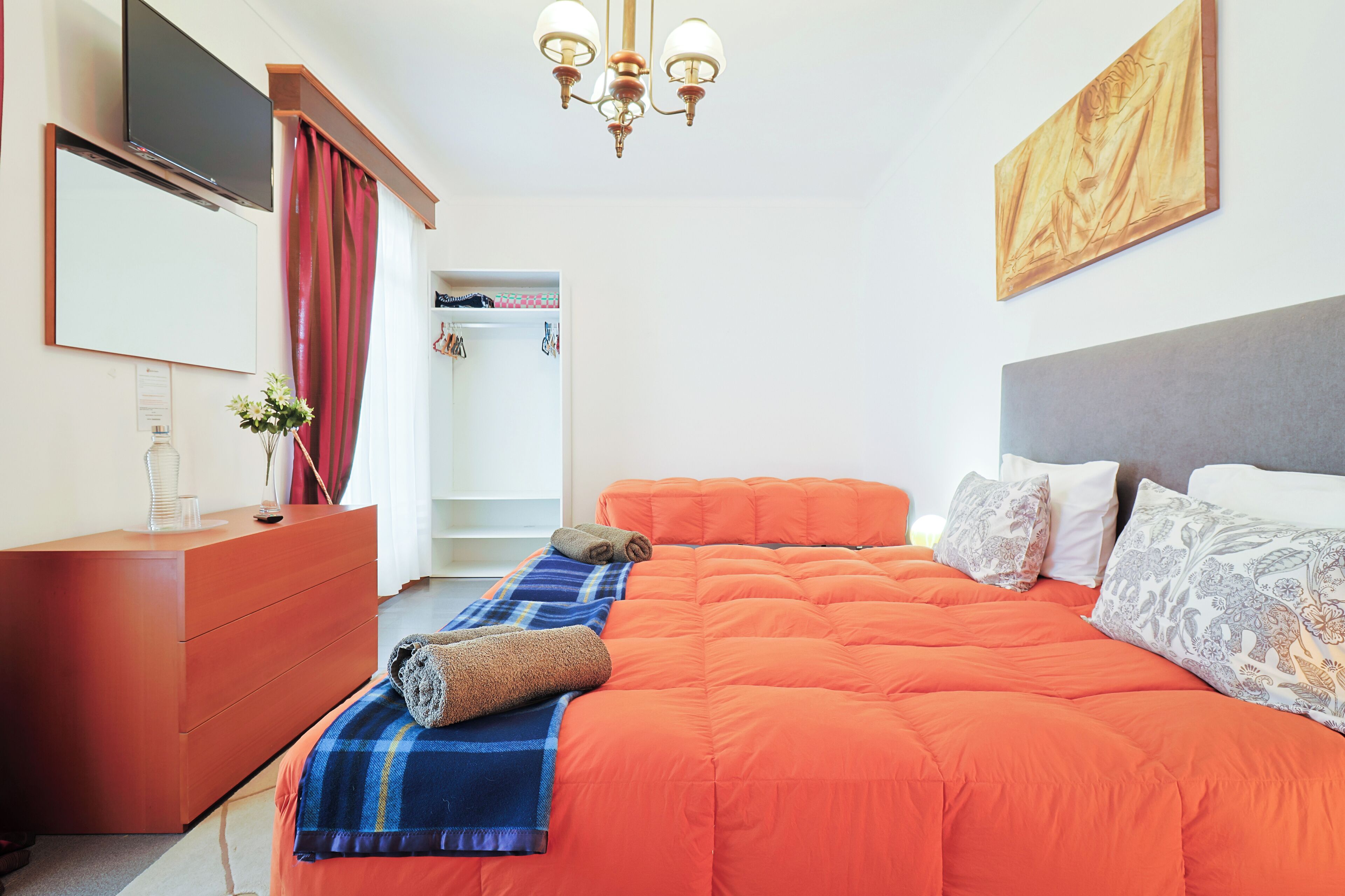 Una camera da letto con un letto arancione, un comò di legno, una TV e un lampadario.