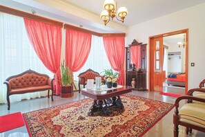 Une pièce spacieuse avec un grand rideau rouge, un canapé en bois, une table basse ornée d’un vase de fleurs et un tapis rouge.