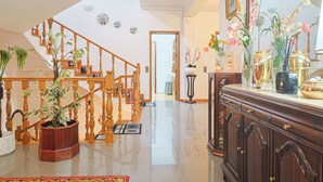 A spacious living area with a wooden staircase, a polished floor, and a large wooden cabinet with decorative items.
