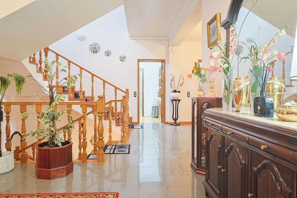 Un vaste espace de vie agrémenté d’un escalier en bois, d’un parquet ciré et d’une grande armoire en bois contenant des objets décoratifs.