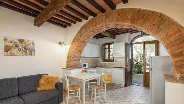 Una cocina con arco de ladrillo, armarios blancos, una mesa de comedor con sillas y un sofá con cojín.