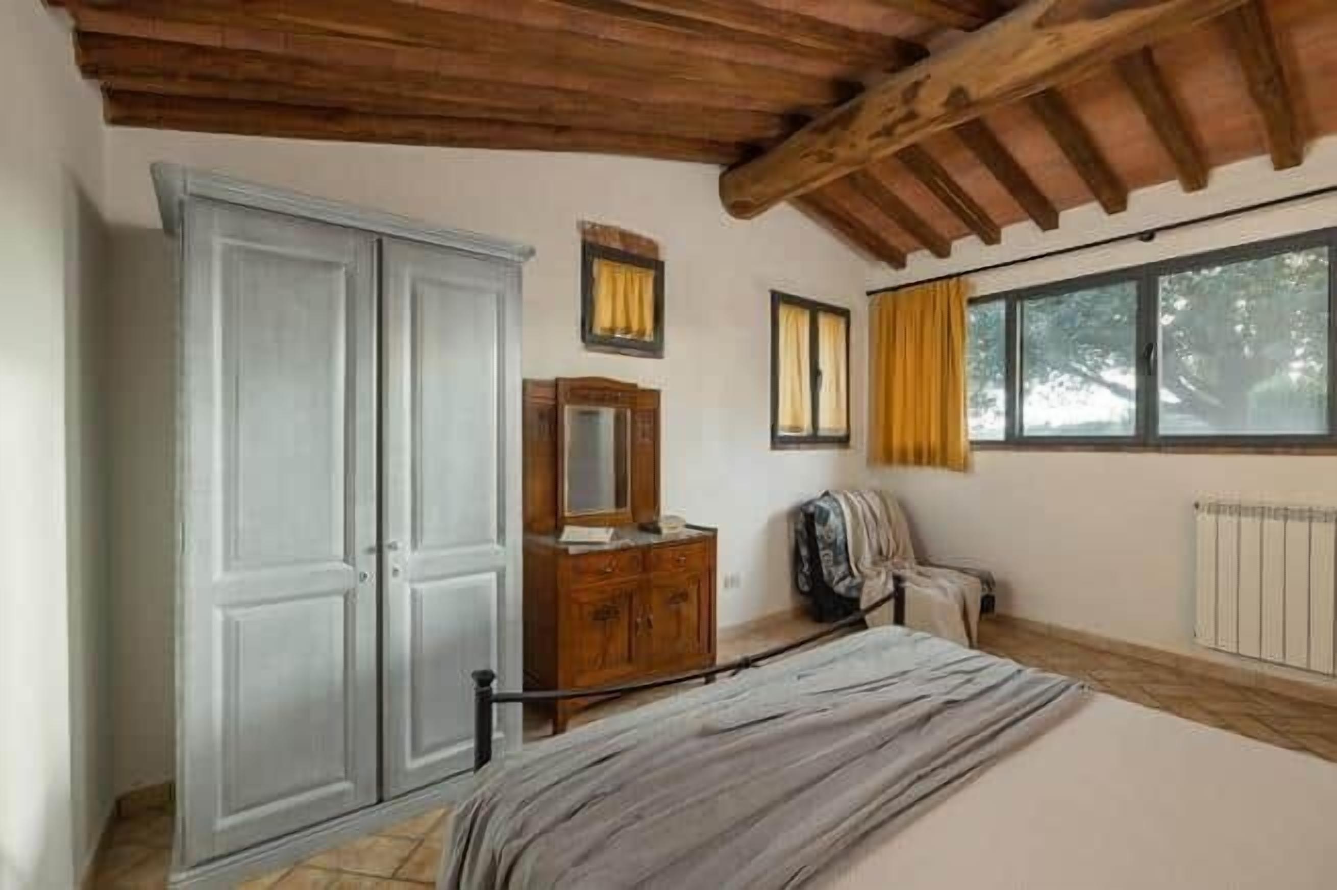 Een slaapkamer met een bed, een kledingkast, een dressoir en een raam met gordijnen.