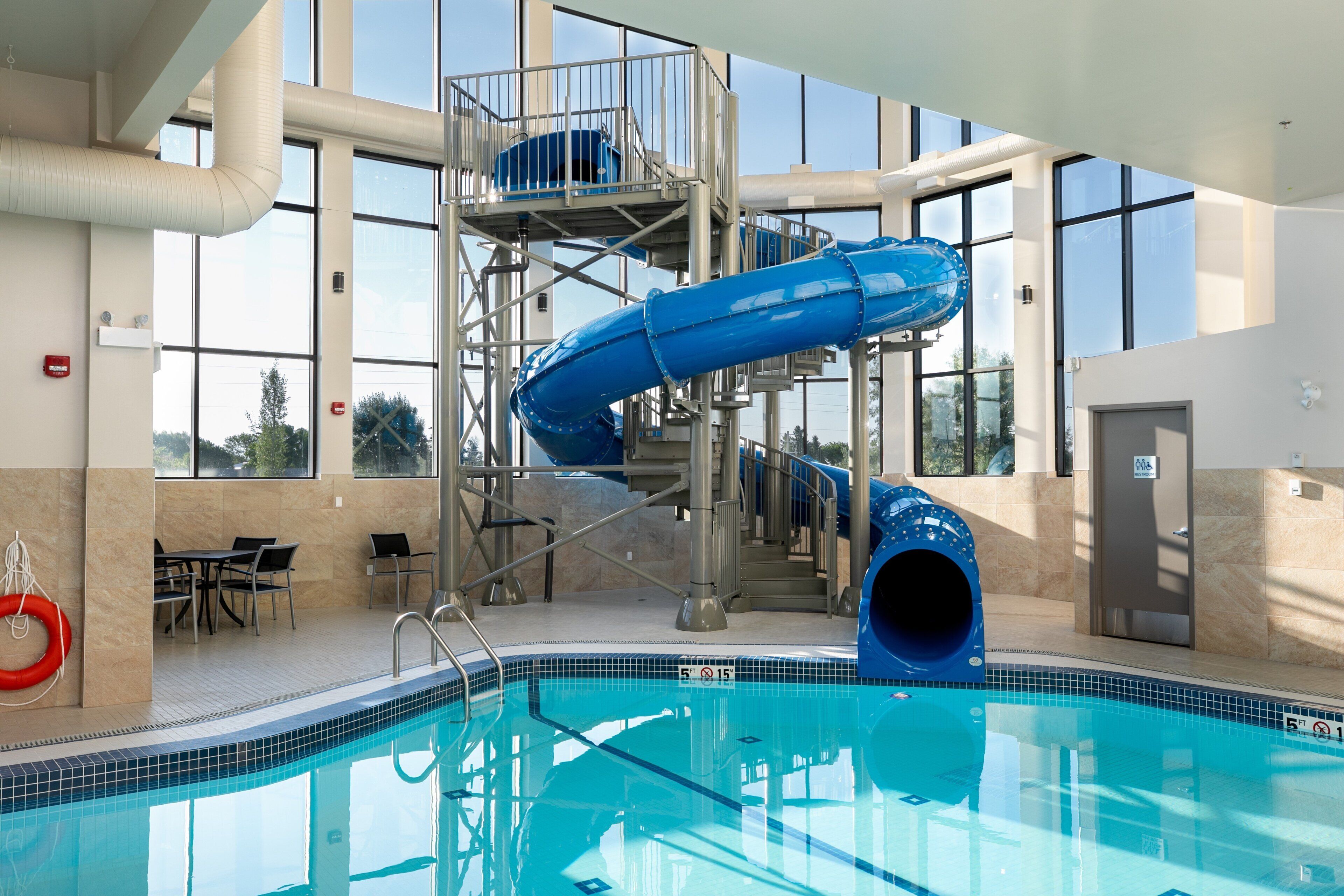 Una piscina interior con un tobogán de color azul, escaleras y un flotador.