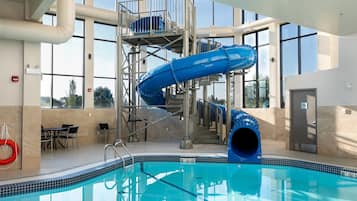 Una piscina interior con un tobogán de color azul, escaleras y un flotador.