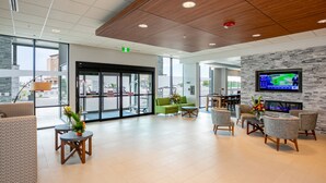 A spacious lobby with comfortable seating, a fireplace, and a large screen displaying a weather forecast. - Holiday Inn Express Lethbridge Southeast by IHG (Lethbridge)