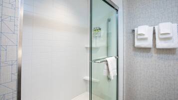 A modern bathroom with a glass shower enclosure, white tiled walls, and a glass door. There are two white towels hanging on a towel rack.