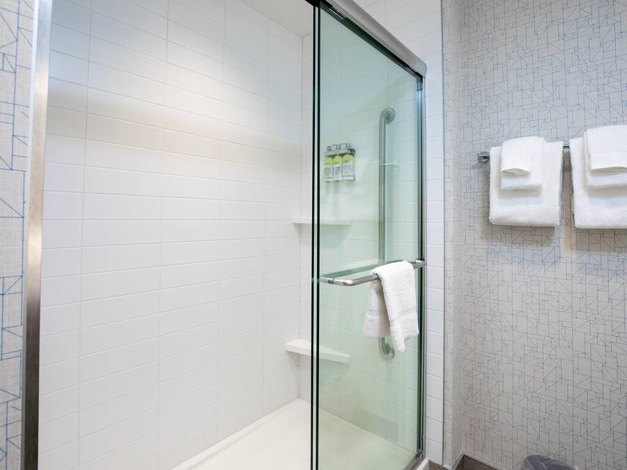 A modern bathroom with a glass shower enclosure, white tiled walls, and a glass door. There are two white towels hanging on a towel rack.