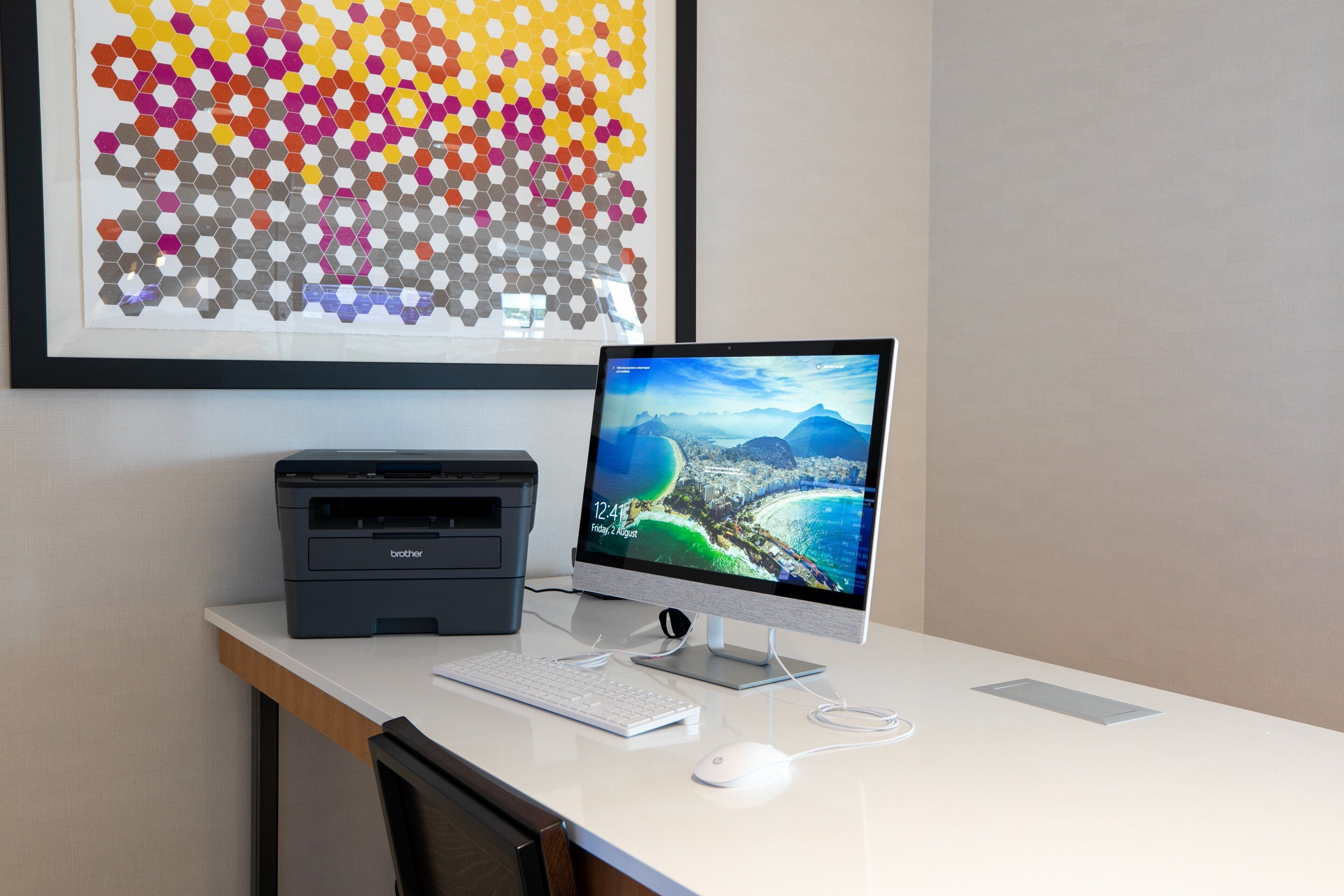 A desktop computer with a monitor displaying a scenic landscape, a printer, and a keyboard on a desk.