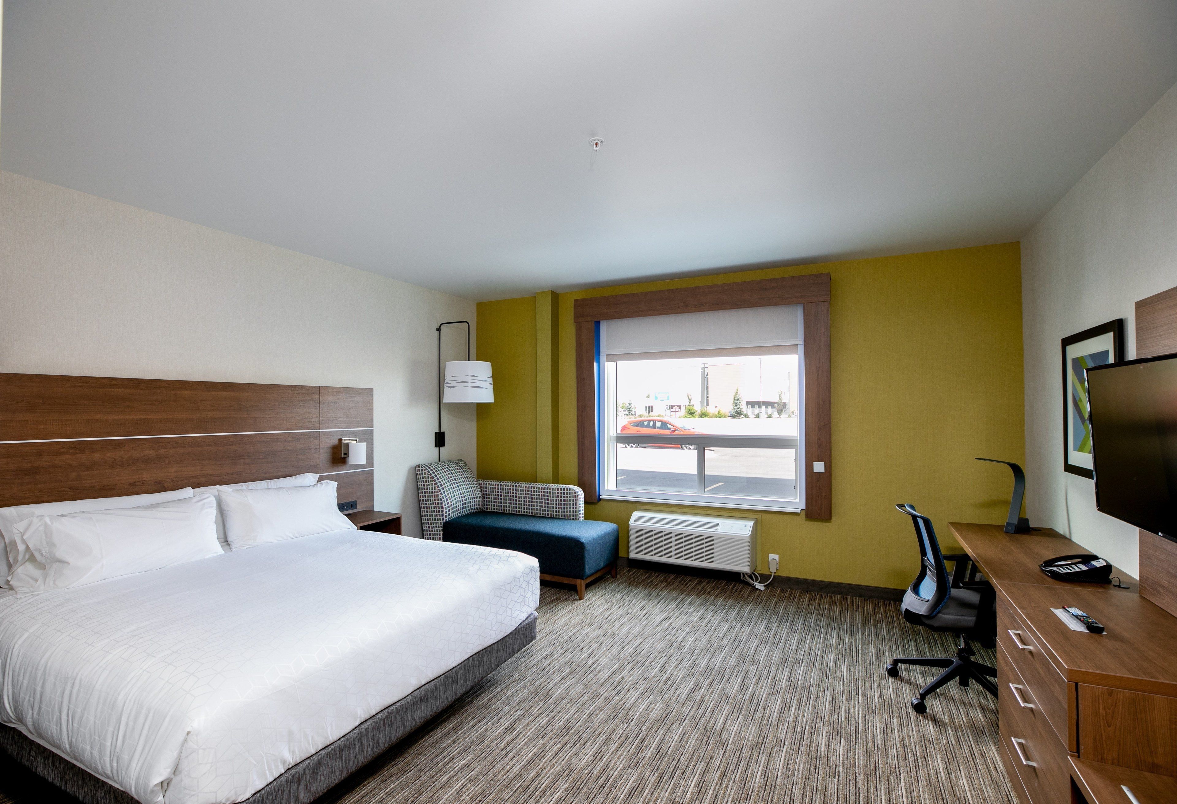 A hotel room with a large bed, a desk, a chair, a sofa, and a window with a view of the street.