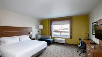 A hotel room with a large bed, a desk, a chair, a sofa, and a window with a view of the street.